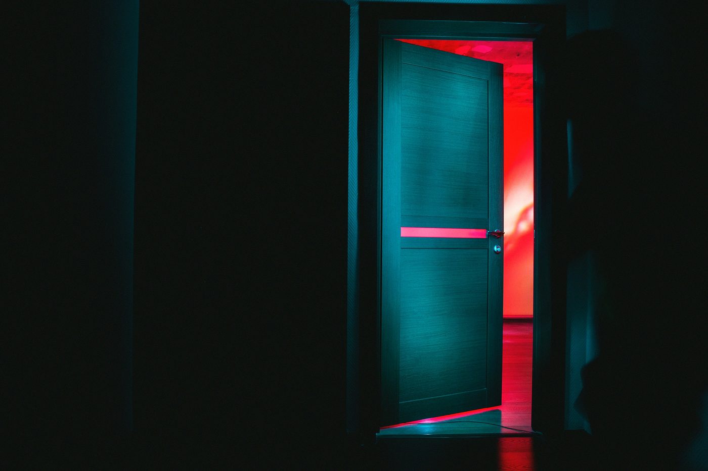 A door ajar in a dark room, red light spilling through